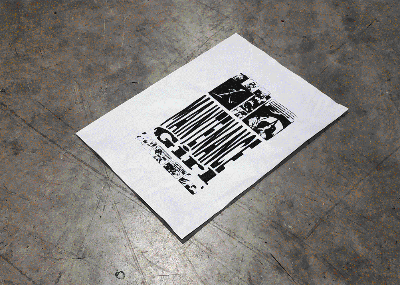 a piece of newsprint, screenprinted with graphics (stretched text and  comics) in black ink, on a concrete floor.